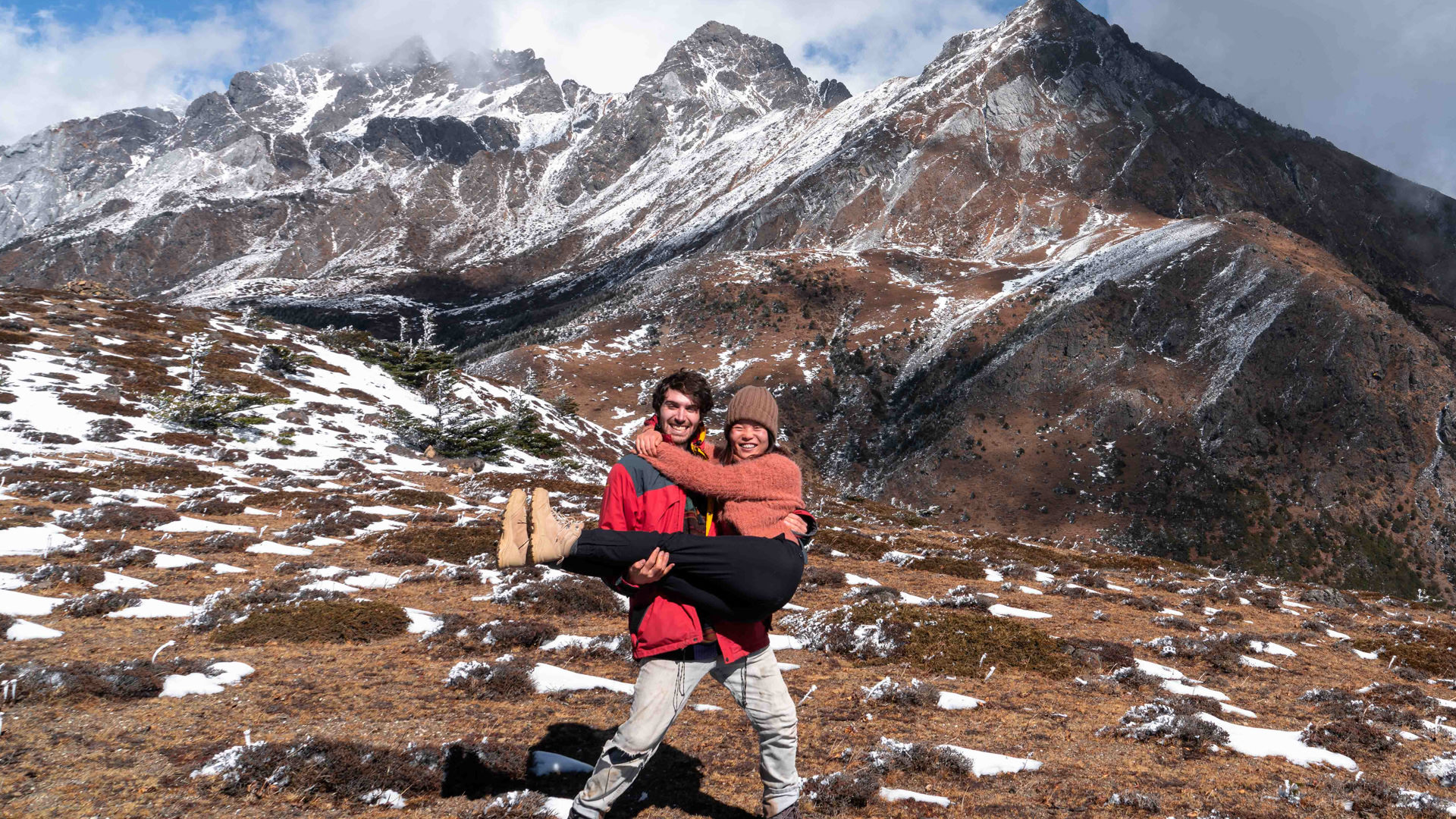 Scott lifts Ella from the ground with the snow-covered peaks of Jade Dragon mountain behind
